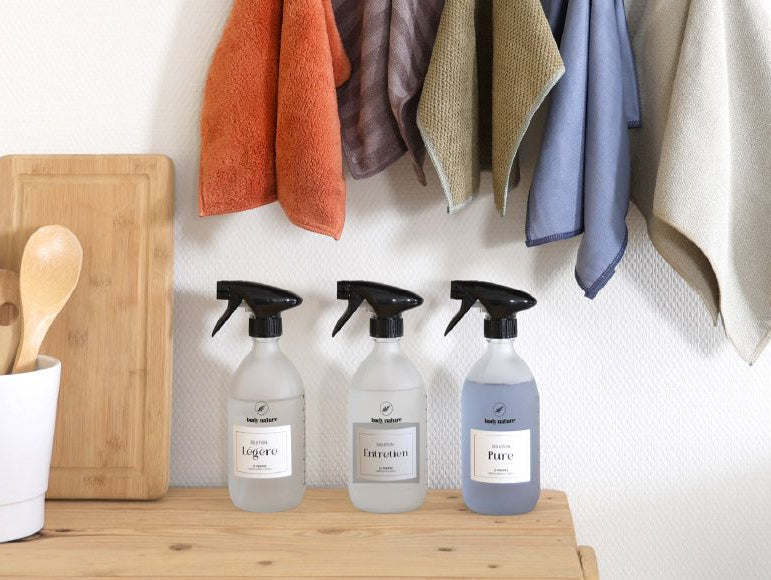 Les 3 flacons du propre poser sur un plan de travaille en bois avec les 5 microfibres accrochés