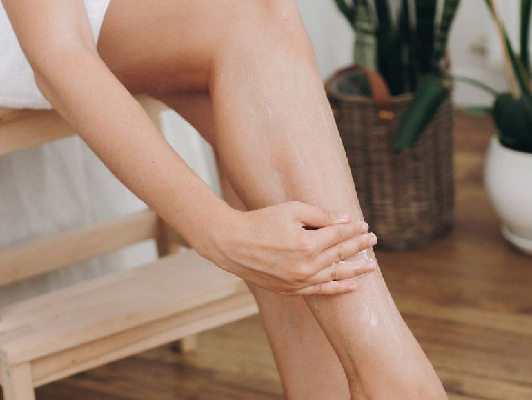 Une jeune femme qui s'applique de la crème sur les jambes assise sur une chaise en bois