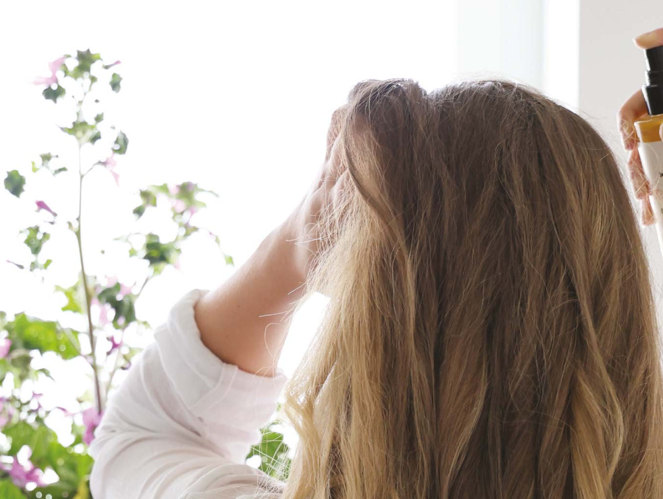 Une femme au long cheveux blond en train d'appliquer une brume pour cheveux