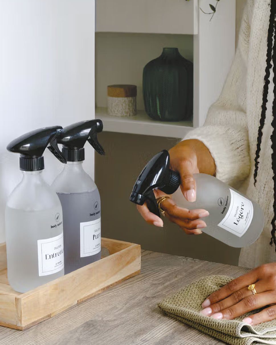 Une main tient un spray dirigé vers une table, une autre main tient un chiffon posé sur la table