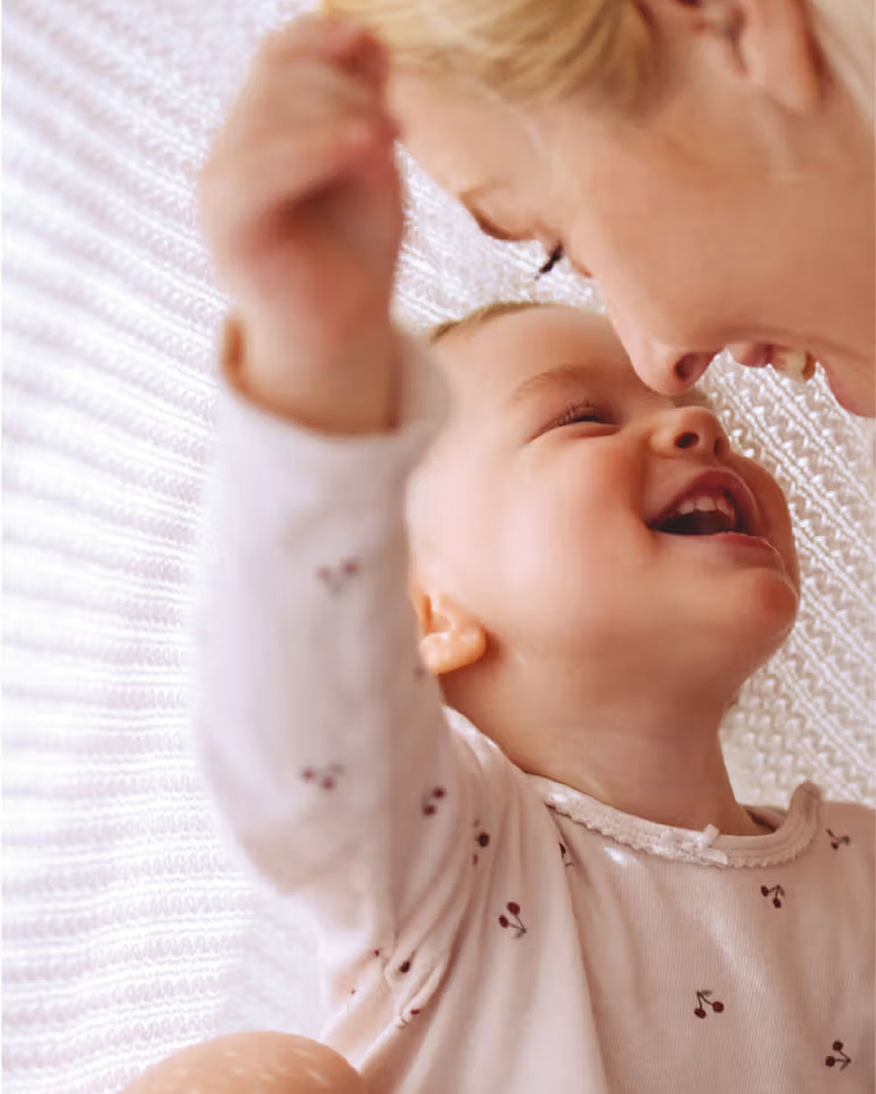 Un bébé souris et tient la tête de sa maman dans ses mains