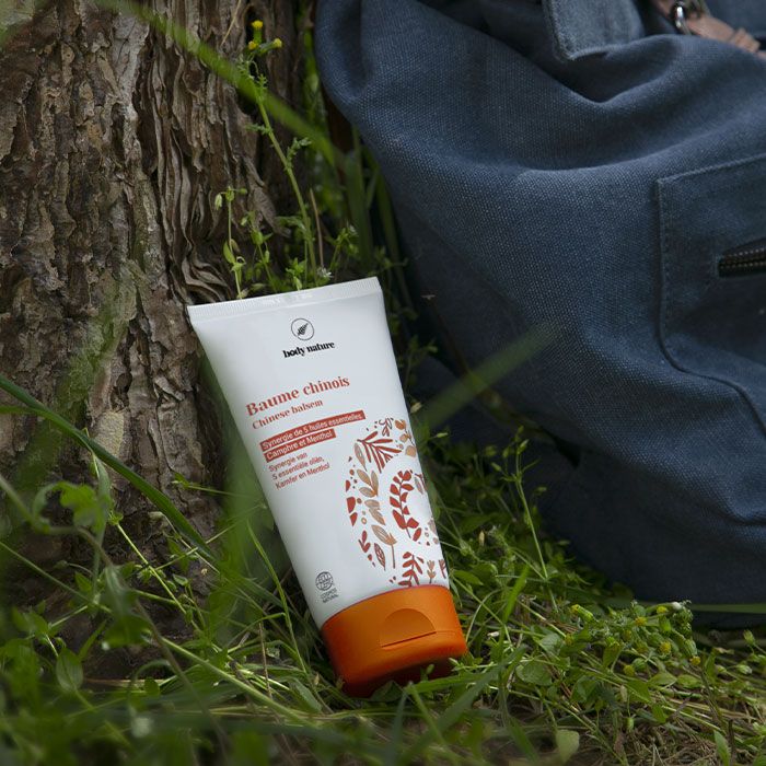 Baume massant chinois pour le bien-être après le sport. Mise en scène : le Baume chinois est posé contre un arbre, dans l'herbe à côté d'un sac.