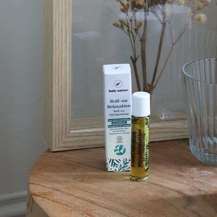 Roll-on relaxant aux huiles essentielles. Mise en scène : le roll on est posé sur une petite table à côté de son emballage.