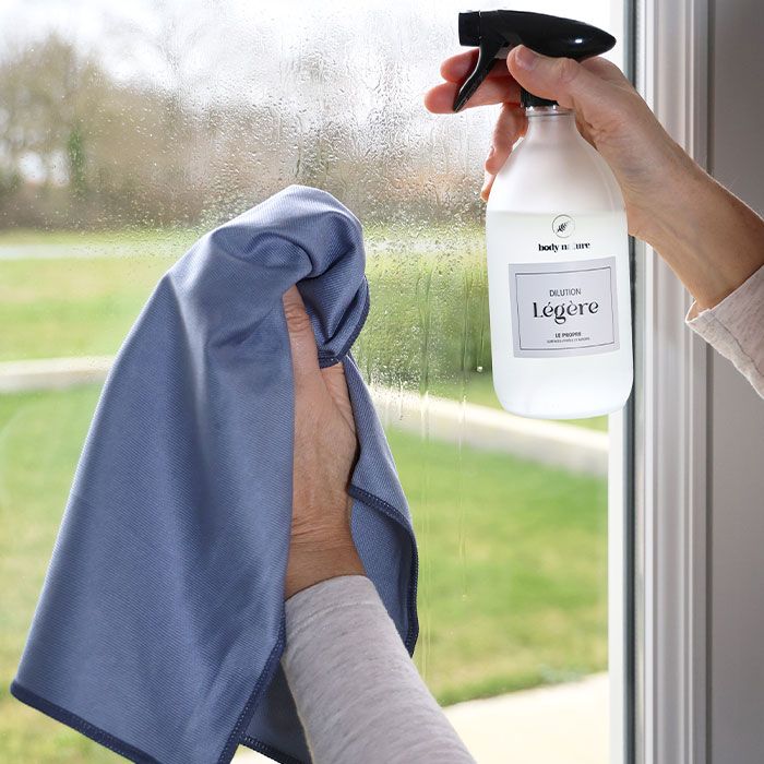 Microfibre spéciale pour le nettoyage des vitres, sans laisser de traces. Personne nettoyant une vitre avec la Microfibre vitre Body Nature et le Flacon en verre pour une dilution"Ultra-légère" du Propre.