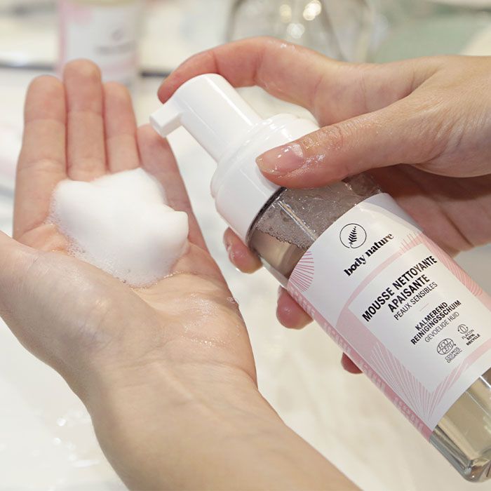 Tube de la Mousse nettoyante et apaisante pour le visage. Mise en scène : push de la pompe, la mousse nettoyante est dans la main d'une personne